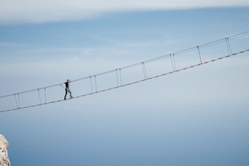 The young man risking life go on rope bridge on sky.