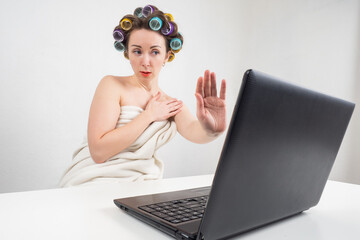 Woman in towels and curlers. Frightened girl in front of computer. She covers laptop camera with...
