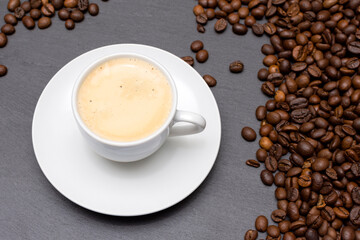 white cup with espresso coffee on a saucer with coffee beans on a dark background