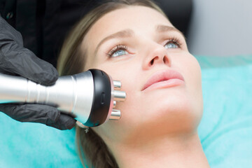 A young woman is lying on the RF-lifting procedure for face skin tightening and face contour...