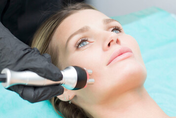 A young woman is lying on the RF-lifting procedure for face skin tightening and face contour...