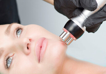 A young woman is lying on the RF-lifting procedure for face skin tightening and face contour...