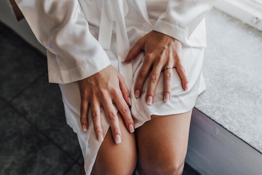 Manos de mujer posadas sobre las rodillas. Manicura de novia el d&iacute;a de su boda. Mujer con bata blanca con manos posando.