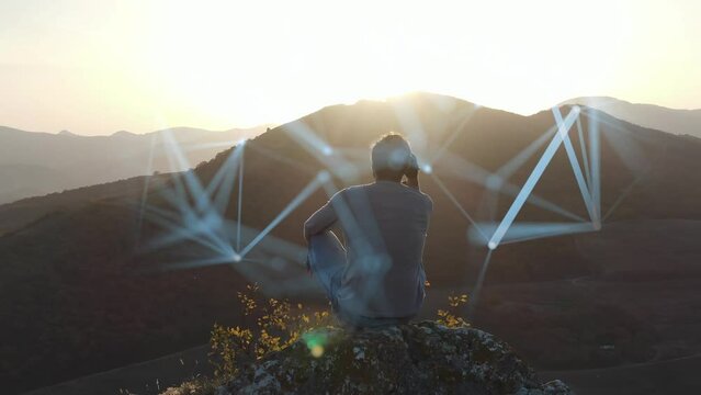 The concept of mental health preservation. A man sits on top of a cliff at sunset and tries to organize his thoughts. The process of concentration is visualized by means of computer graphics