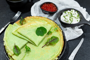 Classic thin pancakes made of green spinach with sour cream and red caviar in a black plate. Top view
