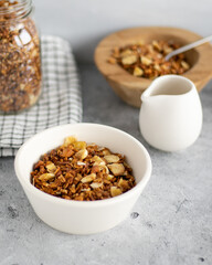Granola in a white bowl neraby jar of granola, wooden bowl with granola and white pitcher on grey background