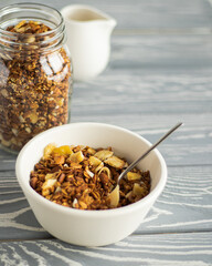 Granola in a white bowl nearby jar of granola and white pitcher on a grey wooden table