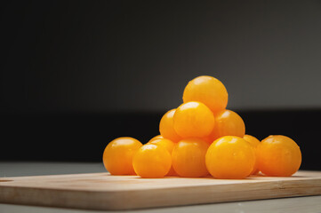 A heap of yellow cherry tomatoes on a wooden cutting board in the kitchen on a white table