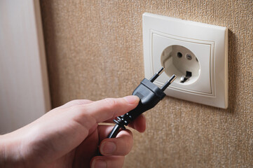 A woman's hand inserts an electric plug into a socket, close-up
