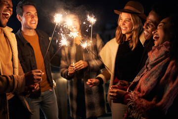Multi-racial group of friends lighting sparklers at a party on a rooftop terrace. Nightlife in the...