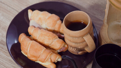 Croissant stuffed with hot dogs Three pieces and black coffee are placed in a plate.