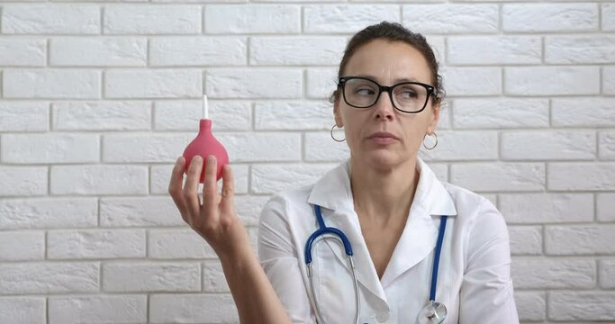 Enema in medical hand. A pensive smiling doctor show and pimping an enema in hand.