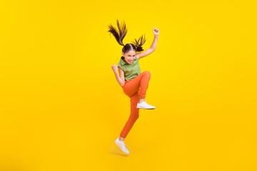 Fototapeta na wymiar Photo of cute lucky preteen girl dressed green top jumping high rising fists smiling isolated yellow color background