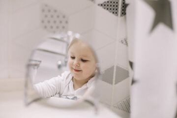 Fototapeta na wymiar little funny girl brushing teeth and washing hands in the bathroom, reflection in the mirror.