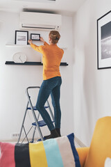 Woman on the ladder hanging pictures and photos on the shelf and wall at home. © astrosystem