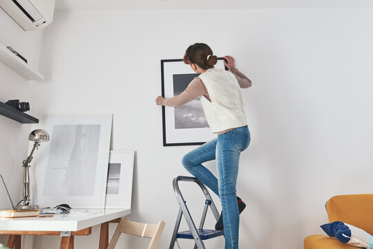 Girl child teenager on the ladder hanging pictures and photos on the shelf and wall at home.