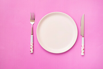 white empty plate and knife with a fork on a pink background