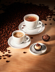 Xícaras com café expresso e Cappuccino, em fundo de madeira com doces e grãos de café torrados
