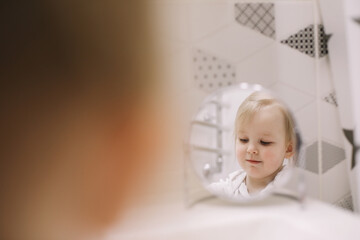 little funny girl brushing teeth and washing hands in the bathroom, reflection in the mirror.