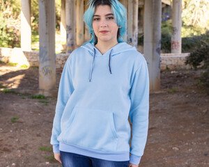 Blue haired Smiling Teenage girl in light blue oversize hoodie stays under bridge