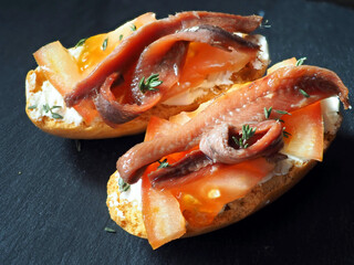 Homemade sandwiches with cream cheese, tomato slices and anchovies on a black wooden table. Close-up