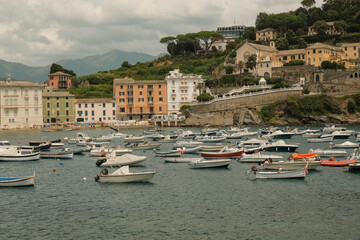 Fototapeta na wymiar boats and yachts floating in the bay of Silence, Baia di Silenzio in Sestre-Levante, Liguria, Italy across the colorful buildings, mountains, and sky. Vacation concept. 