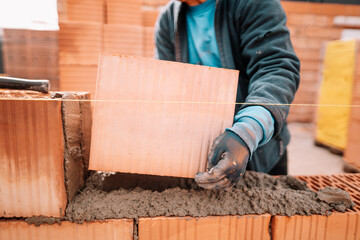 Details of worker hands laying bricks, putty knife, spatula and brick mortar. Construction details at house building
