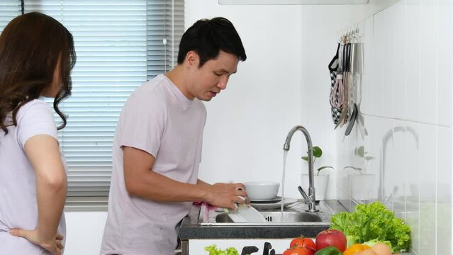 Stressed Young Couple Conflict In Their Kitchen, Angry Woman Pointing Hand To Man For Washing Dishes