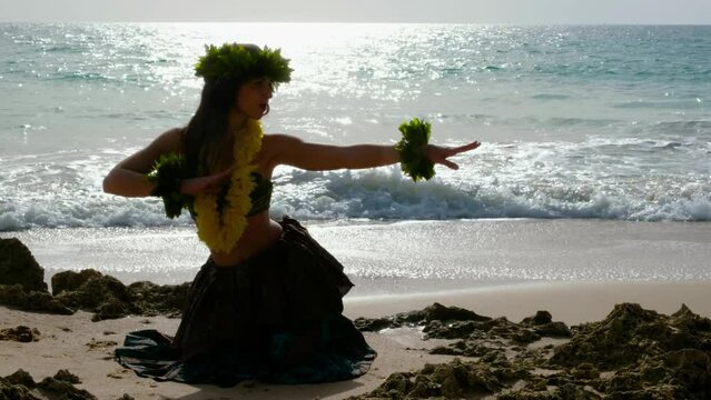 Woman dancing hawaiian hula dance waving her hands on the beach sitting on the sand. Graceful woman dacing hawaiian dance on the beach. Silhouette with blanks. Hula dancer dancing hawaii dance.