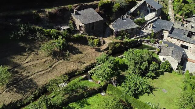 Aerial close shot of a a little town on the valley of the green mountains of Asturias, Spain. Thic forest covering mountain surface under a clear blue sky in pure daylight. Drone moves to the right.