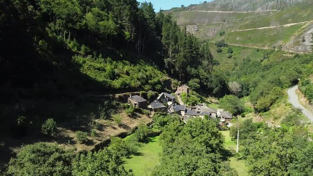 Aerial drone shot of a little town on the valley of the green mountains of Asturias, Spain. Thic forest covering mountain surface under a clear blue sky in pure daylight. Camera gets close.