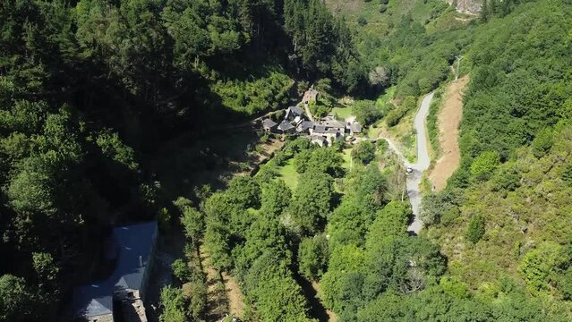 Aerial shot, drone flying over a little town on the valley of the green mountains of Asturias, Spain. Thic forest covering mountain surface under a clear blue sky in pure daylight.