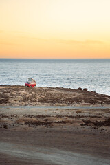 Van Life mit Camper an Küste im Gelände bei Dämmerung am Meer mit orangenem Himmel
