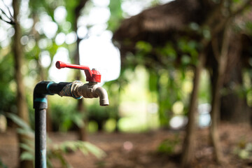 Water faucet tap with valve handle and greenery garden environment as blurred background. Close-up...