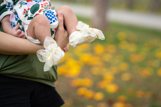 Close-up at mother is holding an infant baby with garden environment and yellow flower as blurred background. People and outdoor scene photo. Selective focus at mother's hand.