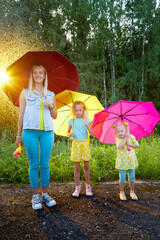 Two cute little blonde girls sisters and mother with umbrellas under rain drops in a summer sunny day. Happy family having rest and fun in good spring day