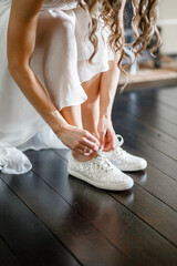 Bride in a white dress tying up her white sneakers Close-up Concept of bridal morning preparations Bridal accessories	Pretty bride in white dress putting on sneakers