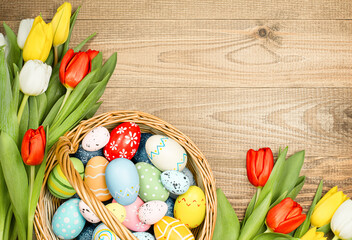 Obraz na płótnie Canvas wicker basket with easter eggs and spring tulips on a wooden table top view