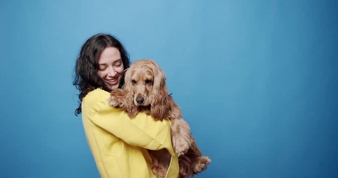 Happy woman have fun with cocker spaniel female dog playing and petting on isolated Blue background. Human animal friendship, Woman playing with her dog. hugs, kiss and pose nicely.