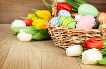 Obraz na płótnie Canvas Easter eggs and tulips in a basket on a wooden table