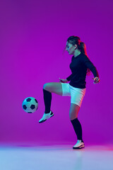 One sportive girl, female soccer player kick in jump football ball isolated on purple studio background in neon light. Sport, action, motion, fitness
