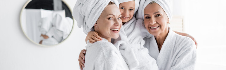 Positive lesbian mothers in bathrobes holding adopted daughter in bathroom, banner