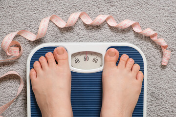 Women's bare feet on floor scales and the number 51 kilograms on the scale, a centimeter tape. The...