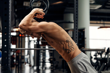 Muscle-up exercise young man doing intense cross fit workout at the gym on gymnastic rings.