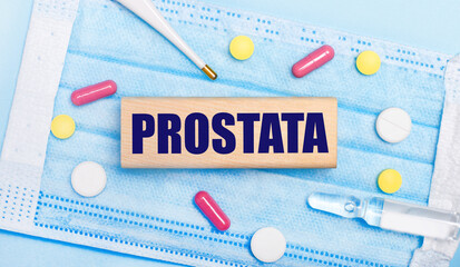 On a light blue disposable face mask there are tablets, a thermometer, an ampoule and a wooden...