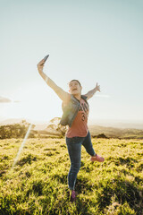 Fototapeta premium Vertical of a beautiful Caucasian woman outdoors taking a picture with her cell phone jumping very happy in a sunset. 