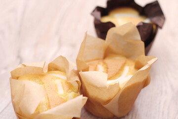 Cupcakes in brown paper cups are placed on a light wooden table.