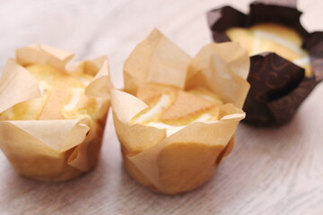 Cupcakes in brown paper cups are placed on a light wooden table.