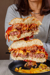 Panino da pub tagliato a metà tra le mani di un cliente con hamburger di carne, pancetta, cheddar fuso e salsa bbq