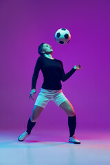 Fototapeta na wymiar Emotive girl, female soccer, football player in motion, action isolated on purple studio background in neon light. Sport, active, healthy lifestyle